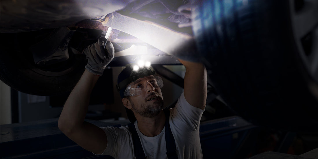 Mechanic wearing gloves working under a car chassis illuminated by a bright Blukar headlamp